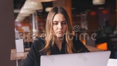 严肃的女商人穿着黑色衬衫在笔记本电脑上工作，在笔记本上记笔记